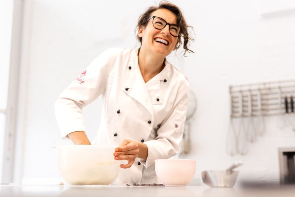 Fröhliche Bäckerin in Konditorei beim Backen, lachend und glücklich.